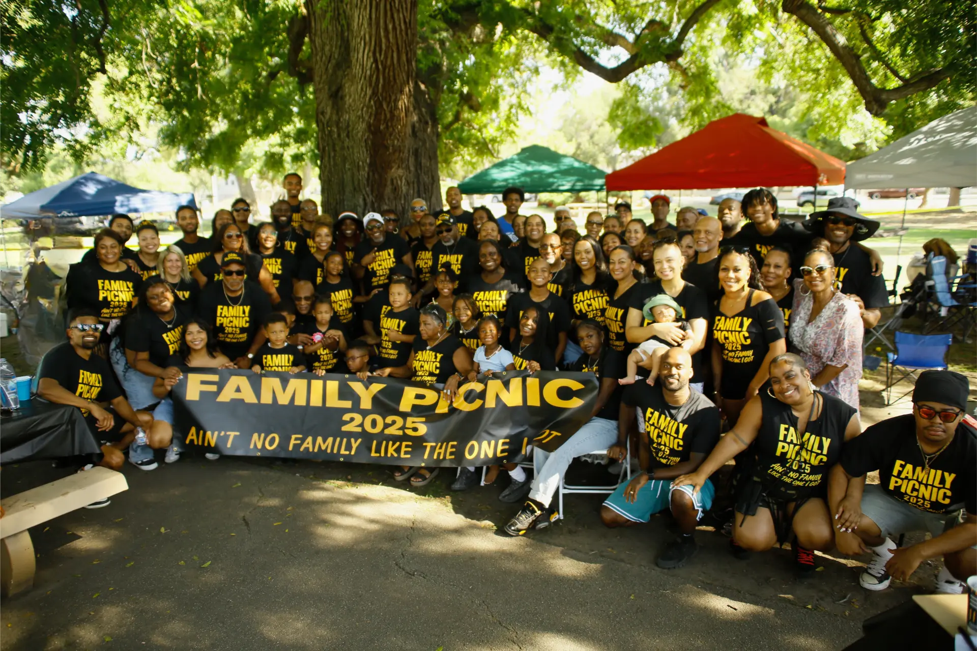 The whole family gathered under the trees behind the Family Picnic 2025 banner